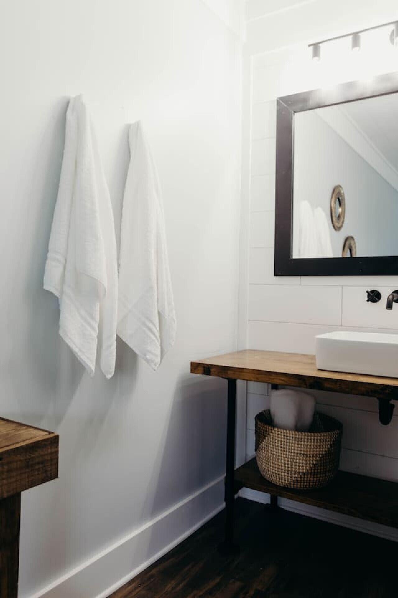 A bathroom with a white sink, a mirror, and two towels hanging on the wall.