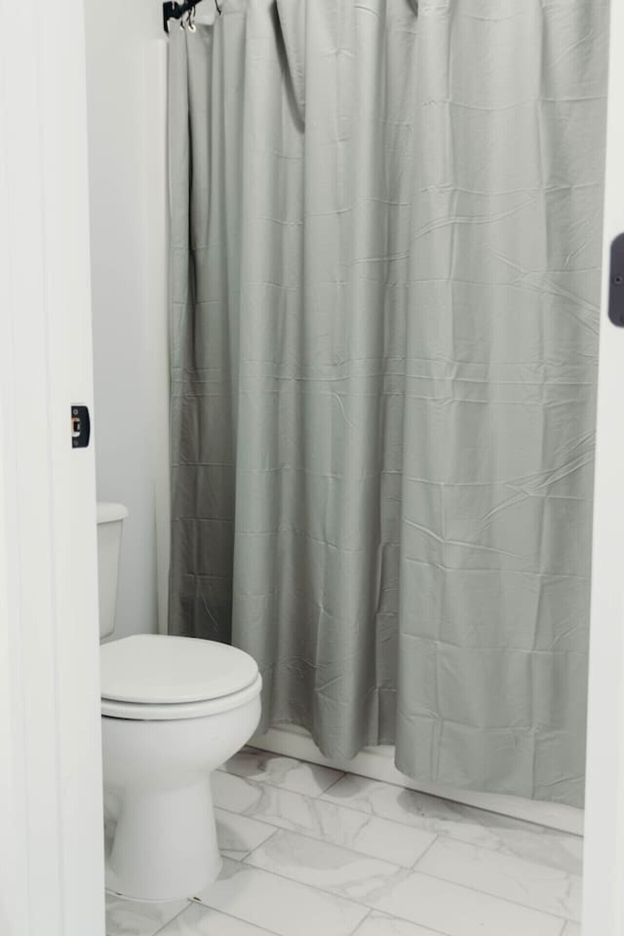 Un baño con inodoro, cortina de ducha y piso de baldosas blancas.