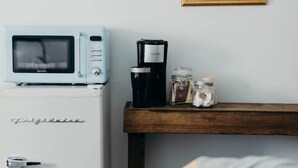 Una kitchenette con un refrigerador blanco, un microondas, una cafetera y un estante de madera con frascos.