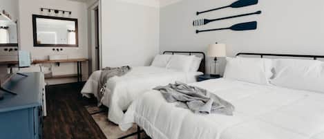 Quarto de hotel com duas camas, uma escrivaninha, um espelho e um objeto decorativo de prancha de remo fixado na parede.