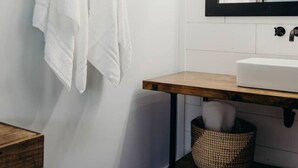 A bathroom with a white sink, wooden countertop, and a mirror. There are two white towels hanging on the wall.