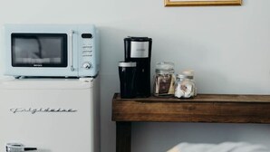 A compact kitchenette with a white refrigerator, a microwave, and a coffee maker on a wooden shelf.