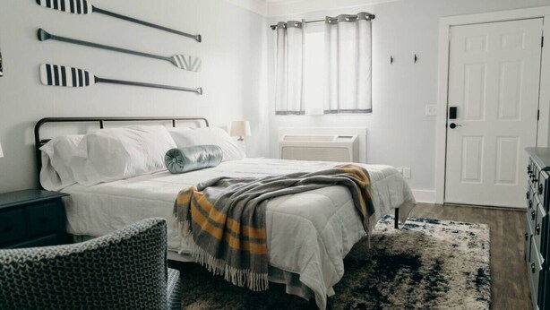 A bedroom with a bed, a bedside table, a chair, a window with curtains, and a door.