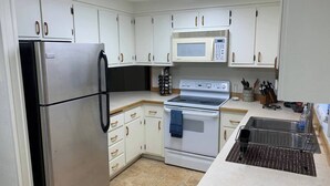 Una cocina con armarios blancos, un refrigerador de acero inoxidable, un microondas, un horno y un lavadero con un escurreplatos.