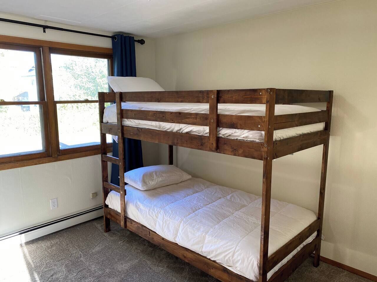 A bunk bed with a ladder, a window with curtains, and a white wall.