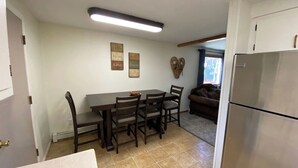 Una cocina compacta con una mesa de comedor, sillas, un refrigerador y una estantería de pared.