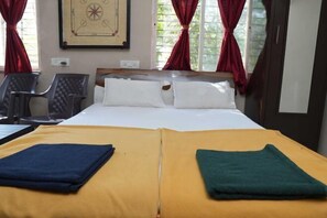 Una habitación de hotel con una cama, dos sillas, un ventanal con cortinas y un cuadro colgado en la pared.