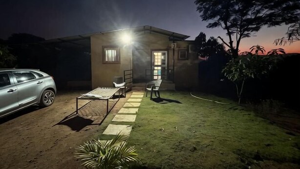 A house with a patio, a car parked outside, and a well-lit entrance. - Bimal Farm Home Stay (Koroli)
