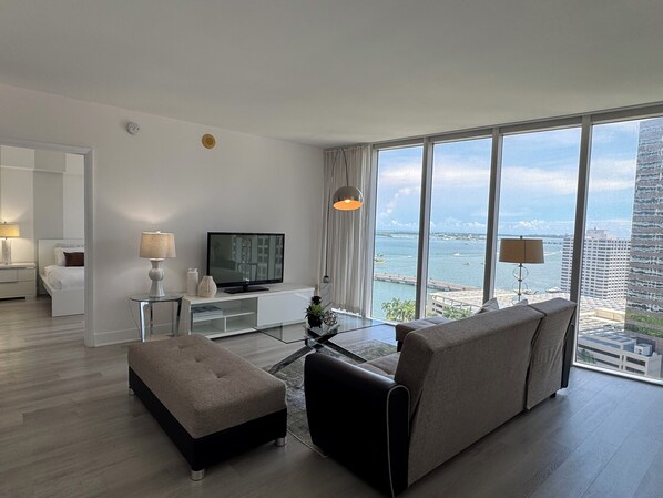 A modern hotel room with a large window offering a view of the city and water.