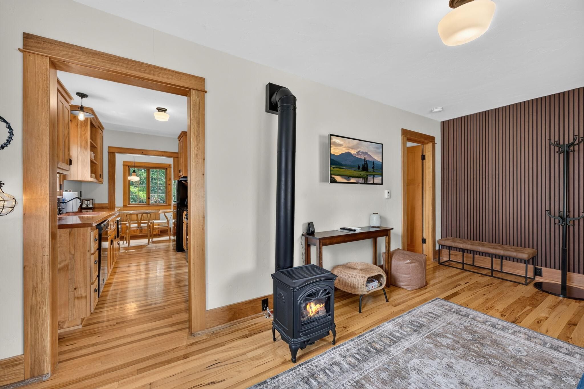 A room with a wood-burning stove, wooden flooring, a dining area, and a view of a mountainous landscape.