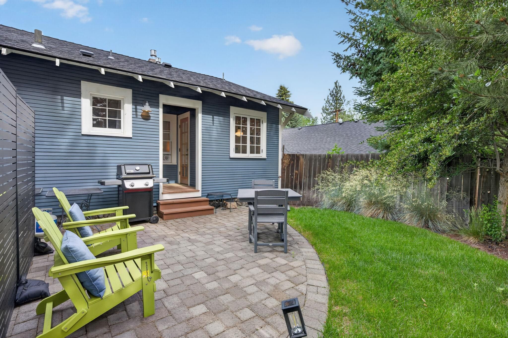 A blue house with a patio, a grill, and a table with chairs.