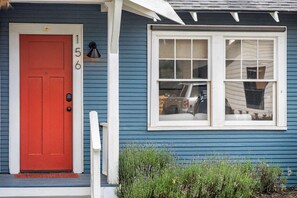 Een blauw huis met een rode deur, een wit raam en een klein portaal met een witte balustrade.