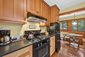 A kitchen with wooden cabinets, a gas stove, a coffee maker, and a dining area with a table and chairs.
