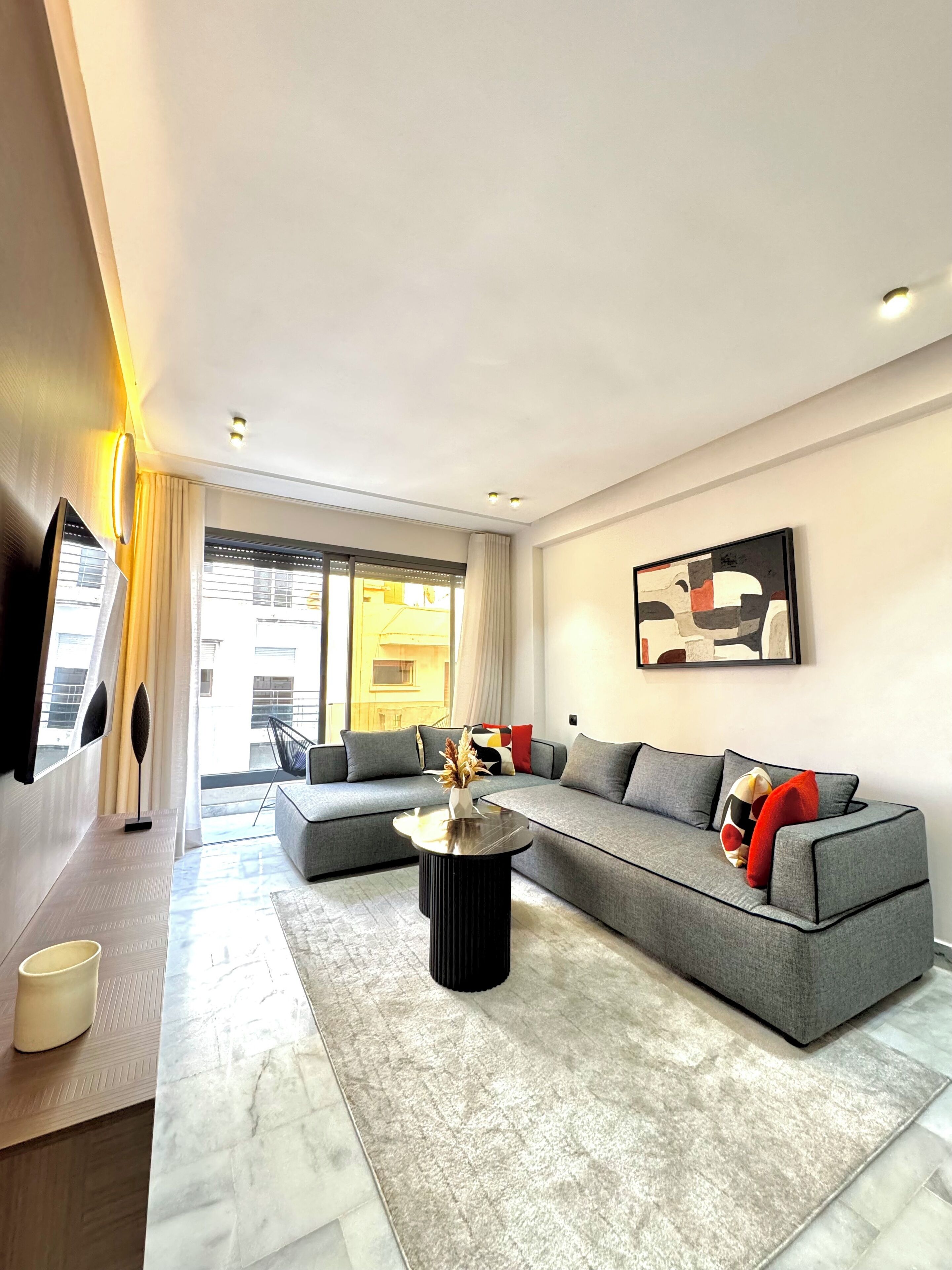 A modern living room with a grey sectional sofa, a black coffee table, and a large window with curtains.