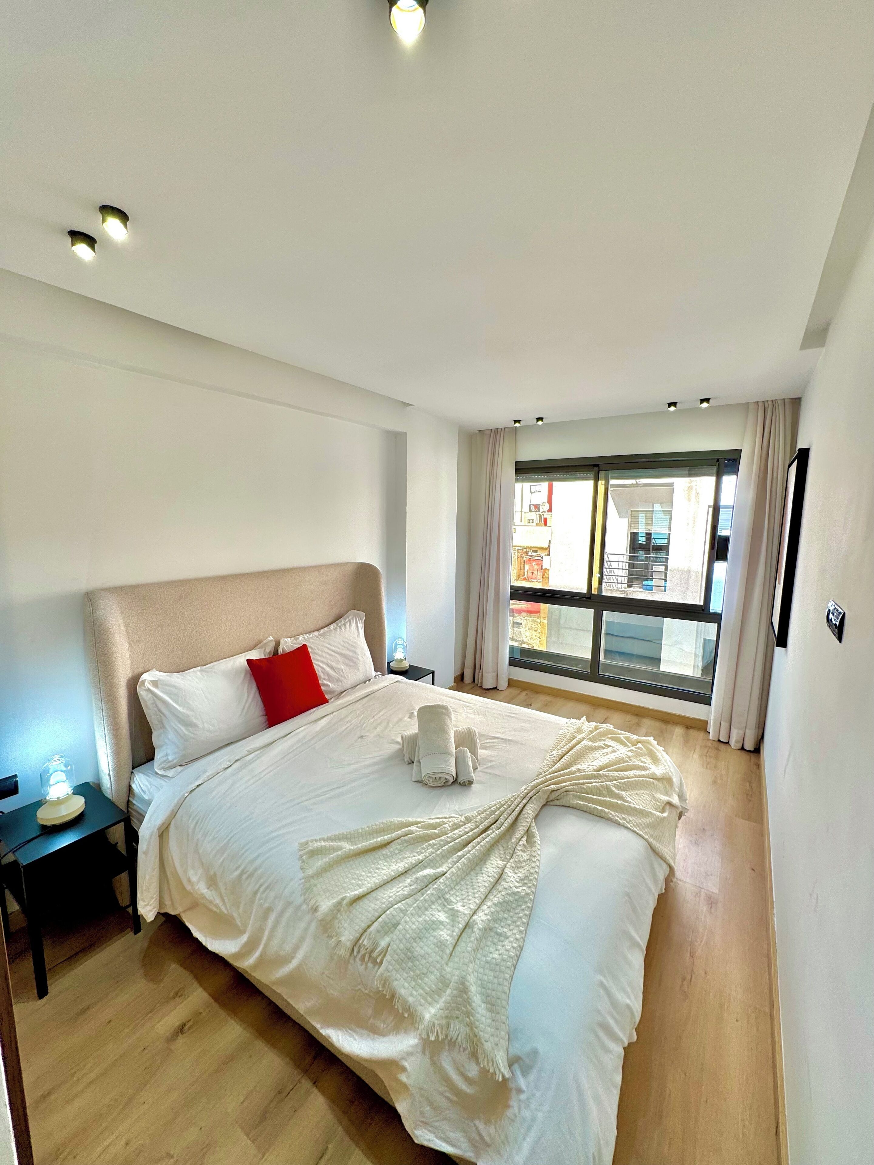 Una habitación de hotel moderna con una cama grande, una mesita de noche y un ventanal con cortinas.