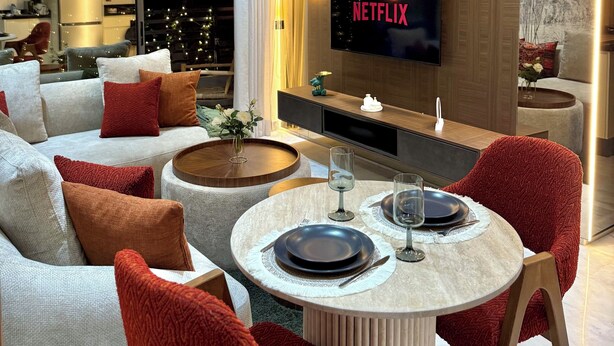 Un salon moderne doté d’un téléviseur à écran plat, d’un ensemble de canapés, d’une table basse et d’un coin repas avec une table dressée pour deux personnes.