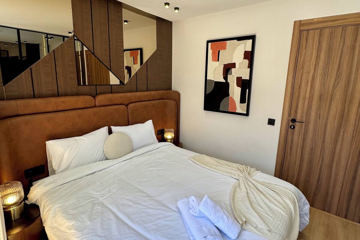 A neatly made bed with white linens, a wooden headboard, and a mirror above it.