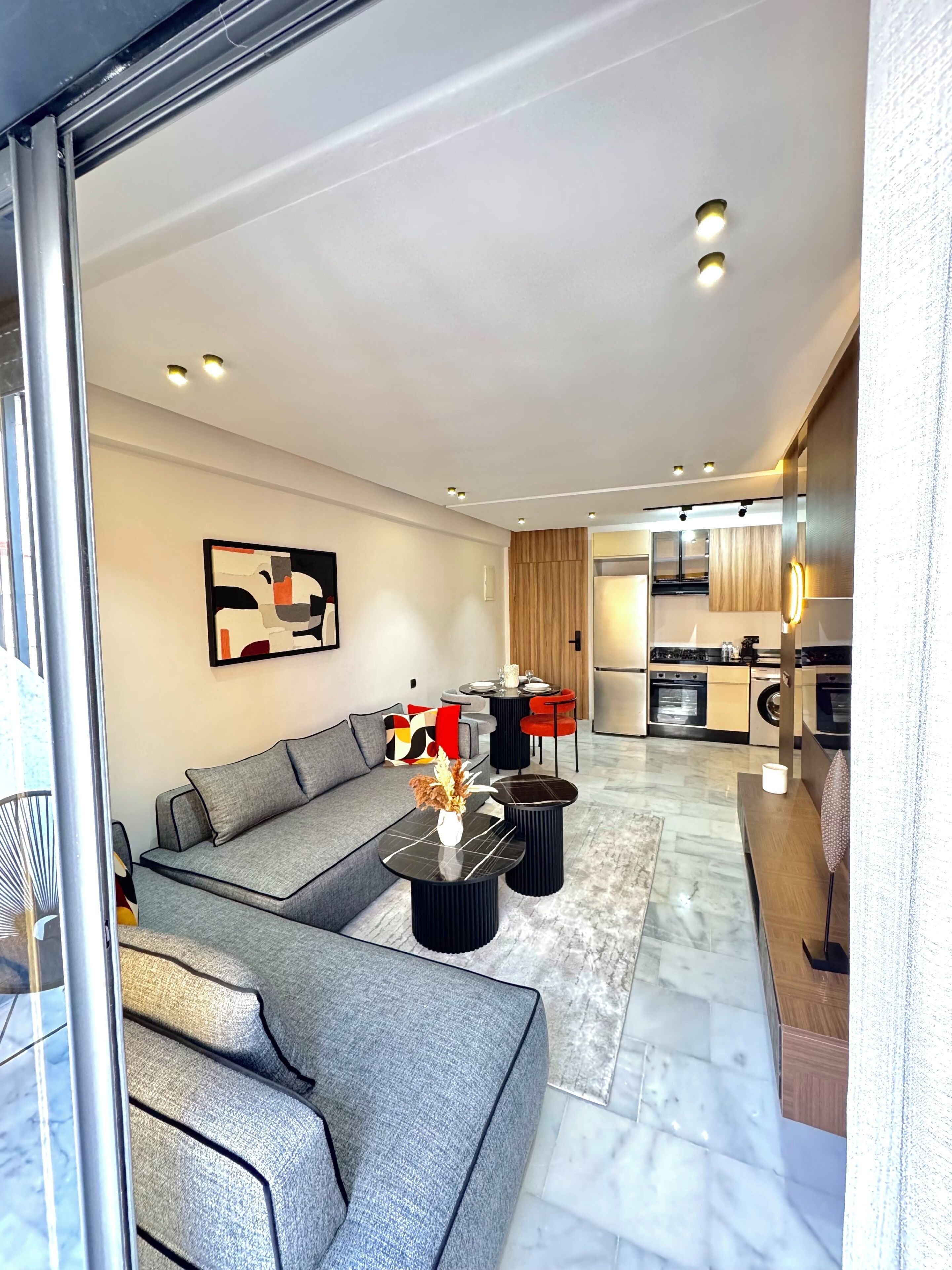 Ein modernes Wohnzimmer mit einem grauen Sofa, einem schwarzen Couchtisch und einem Essbereich mit einem runden Tisch und roten Stühlen.
