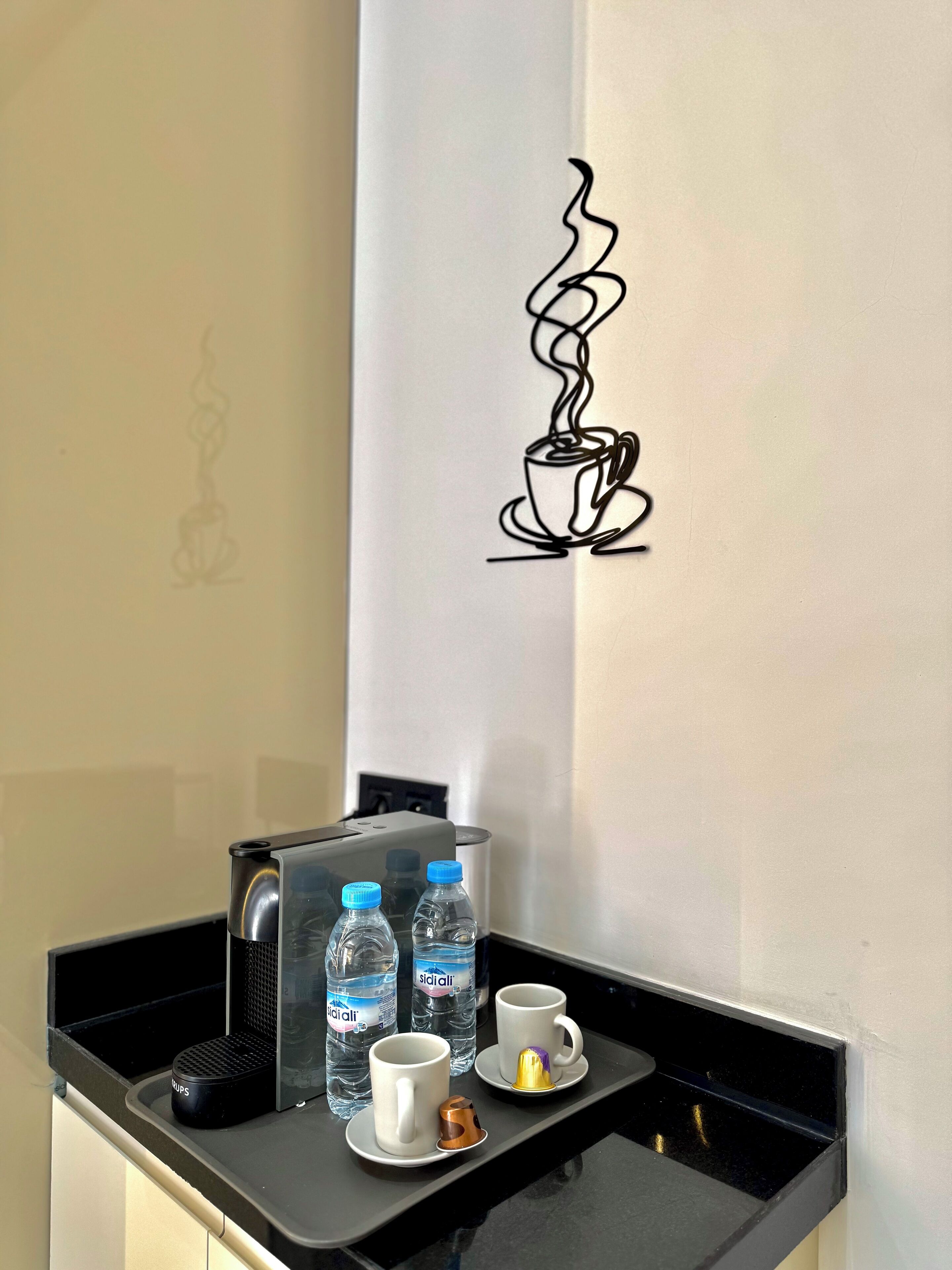 A kitchenette area with a coffee machine, two water bottles, and two cups on a tray.