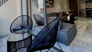 Un salon moderne avec une porte vitrée donnant sur un balcon, un ensemble de canapés et un coin repas avec une cuisine en arrière-plan.