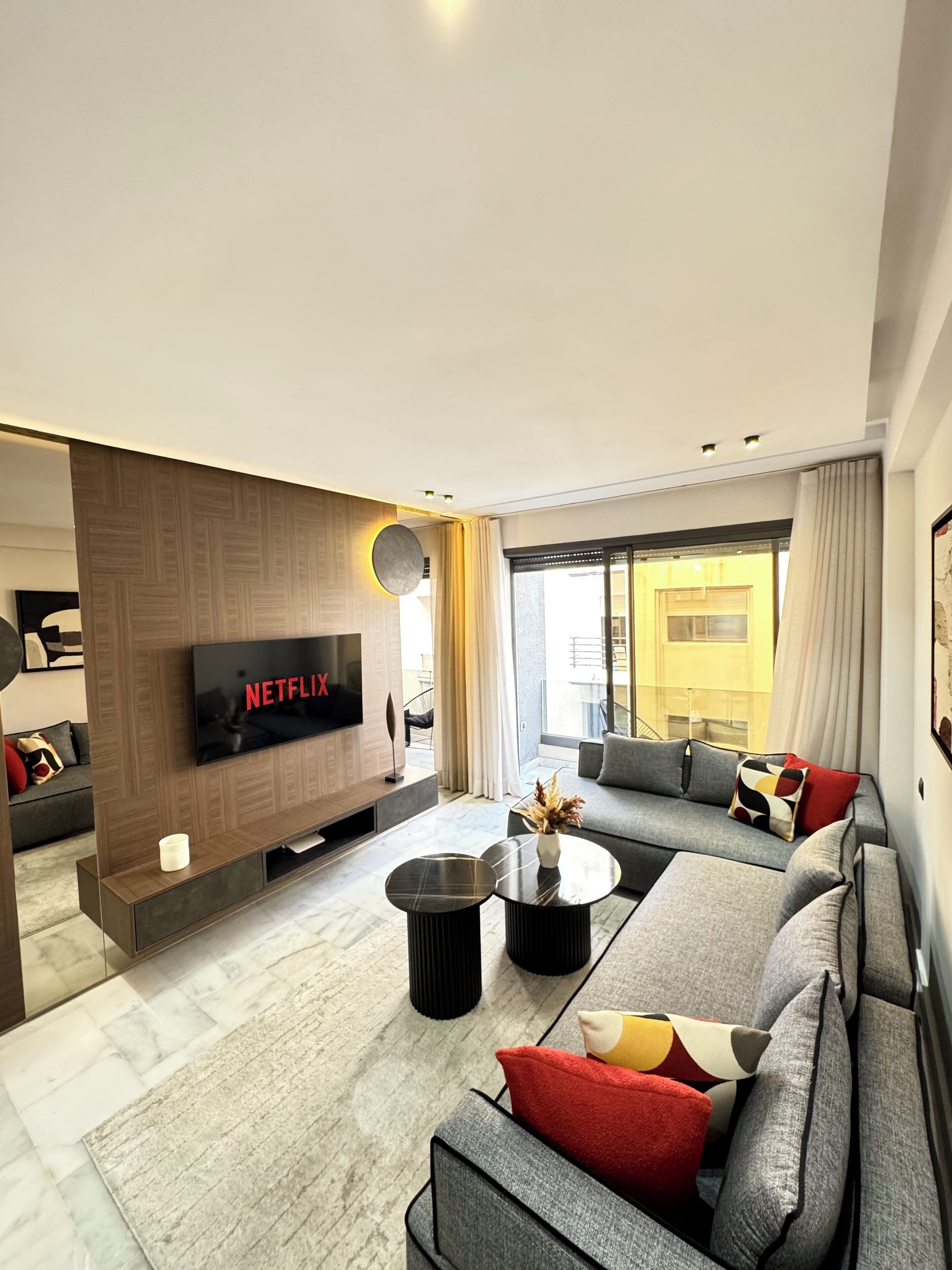 A modern living room with a flat-screen TV, a sofa, a coffee table, and a large window.