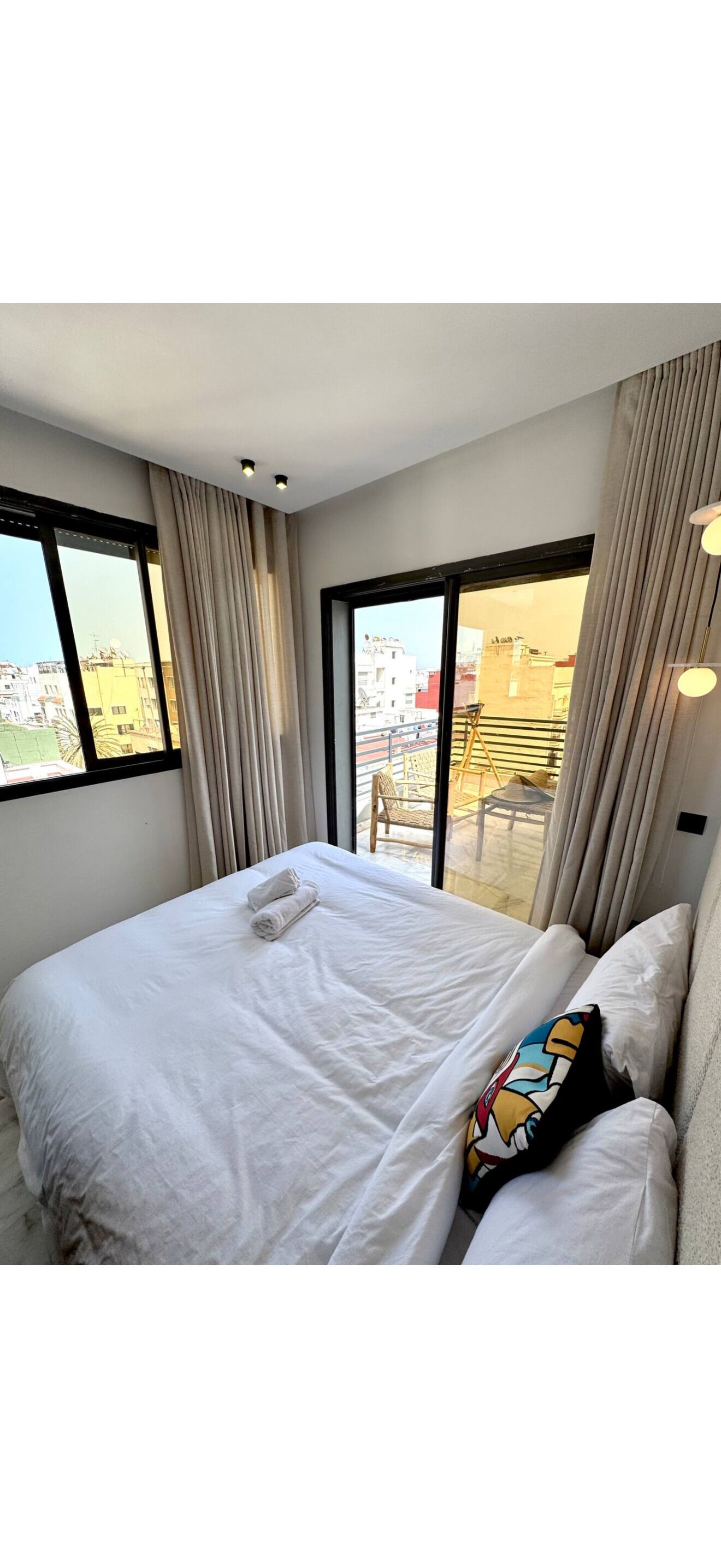 Ein Hotelzimmer mit einem großen Bett, zwei Fenstern und Blick auf die Stadt.