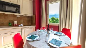 Une table à manger dressée avec des assiettes, des verres et des couverts, et une fenêtre donnant sur un paysage verdoyant et montagneux.