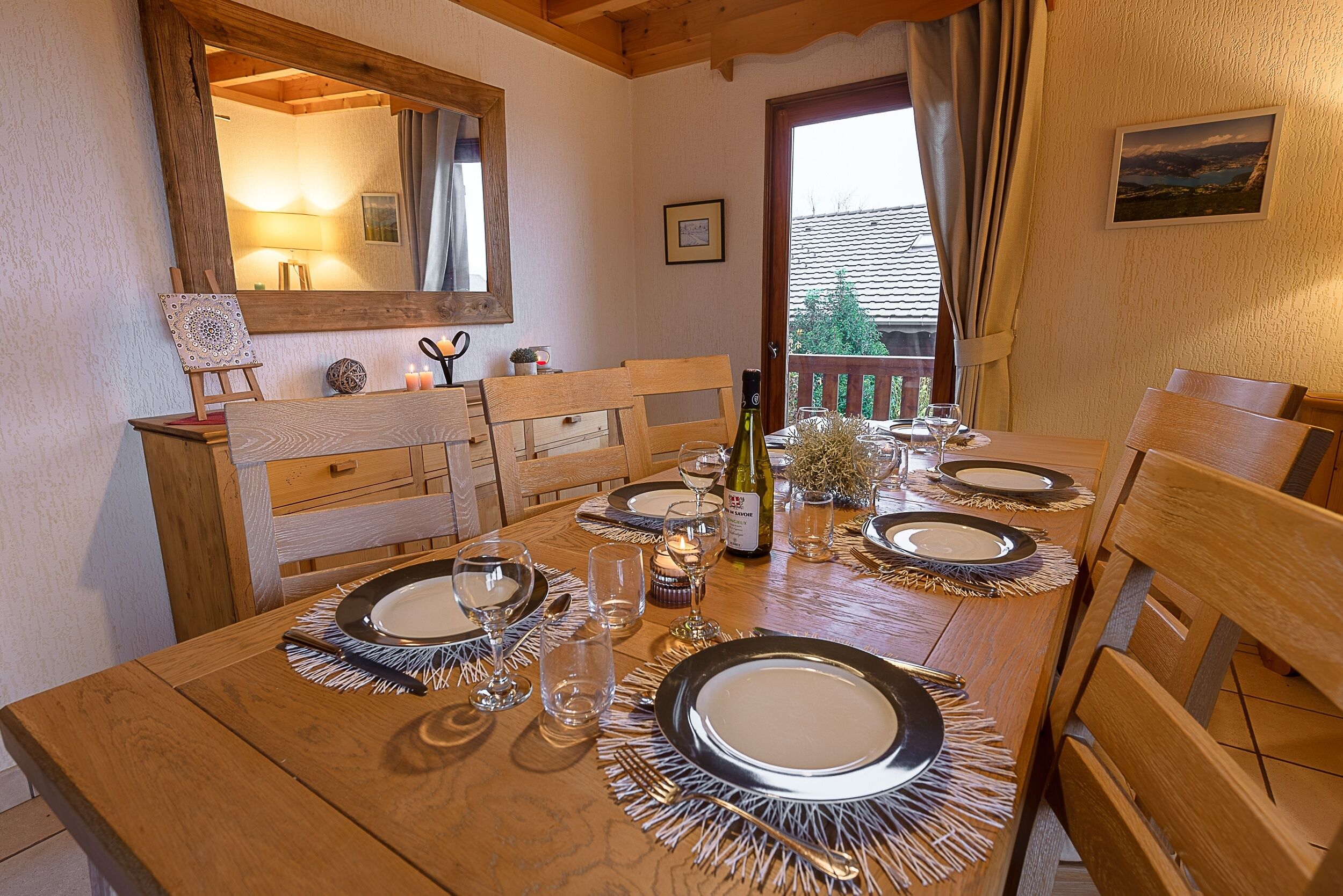A dining table set with plates, cutlery, and candles, with a wooden bench and a mirror on the wall.