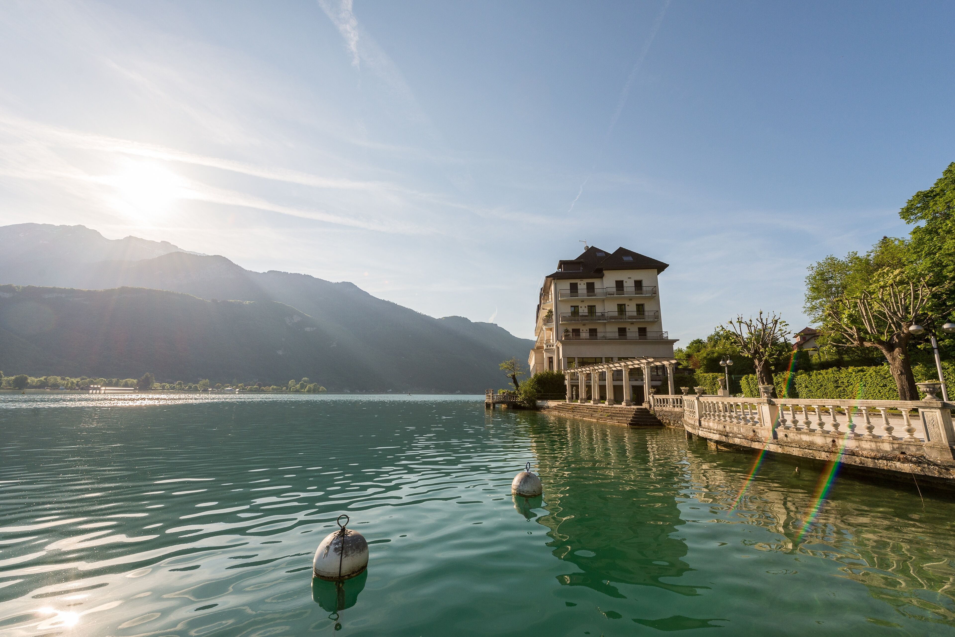 A building with a balcony overlooking a calm lake, surrounded by mountains.