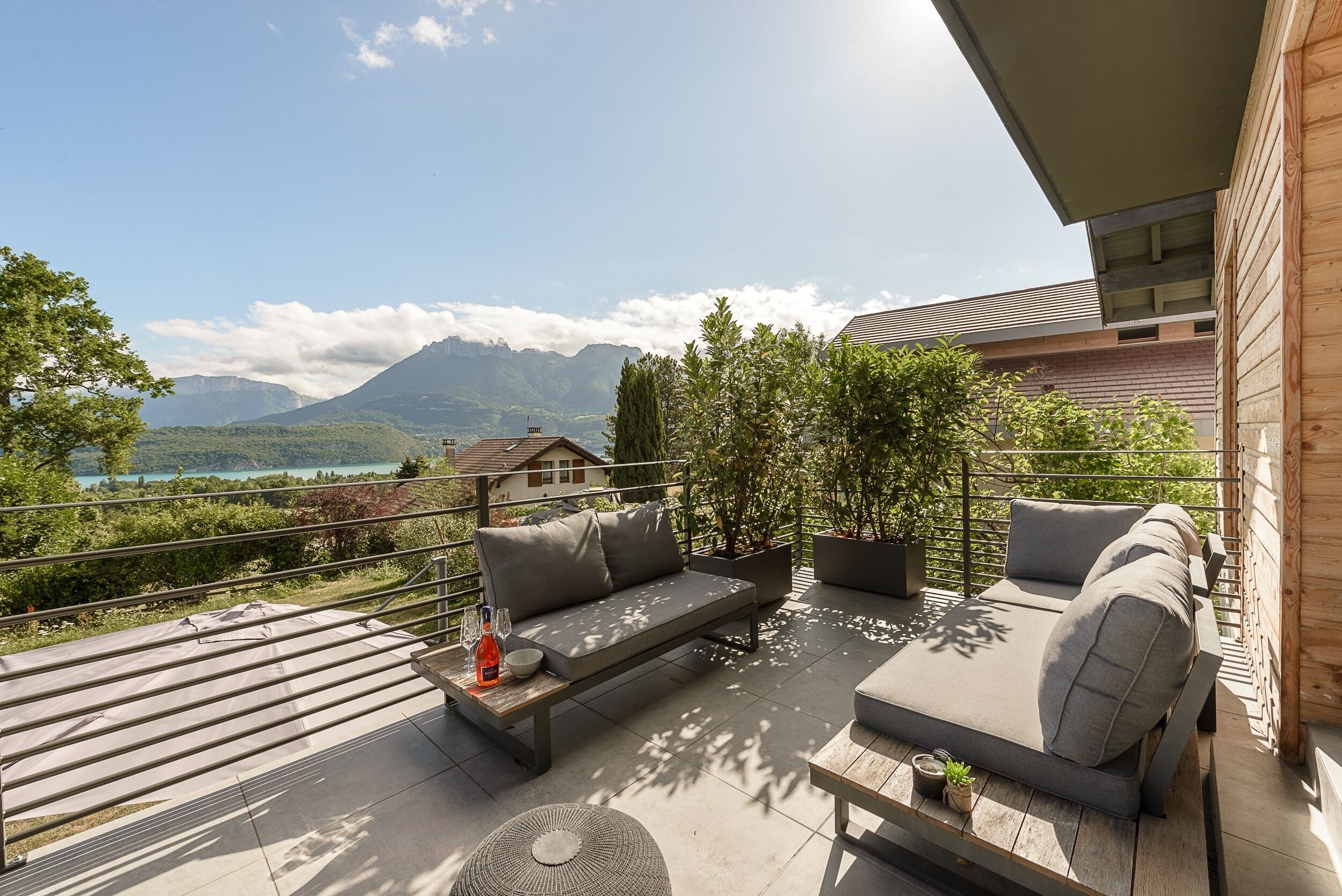 Ein Balkon mit einer Couch und einem Tisch, mit Blick auf eine Berglandschaft und einen See.