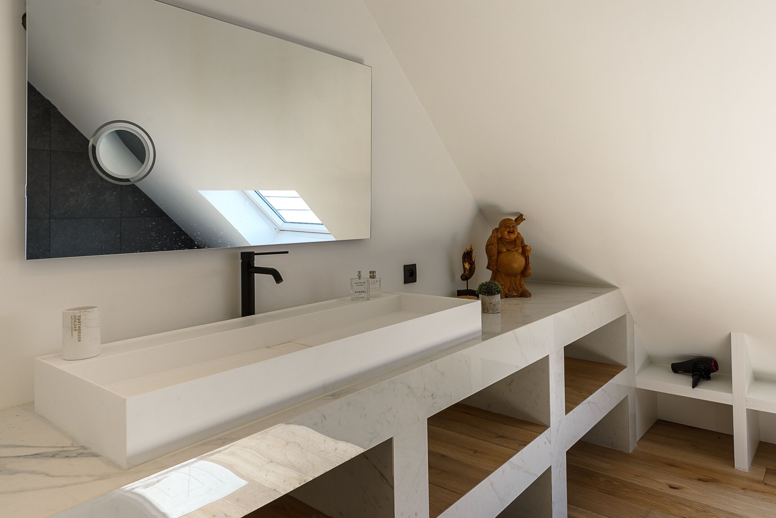 A modern bathroom with a white vanity, a large mirror, and a skylight.