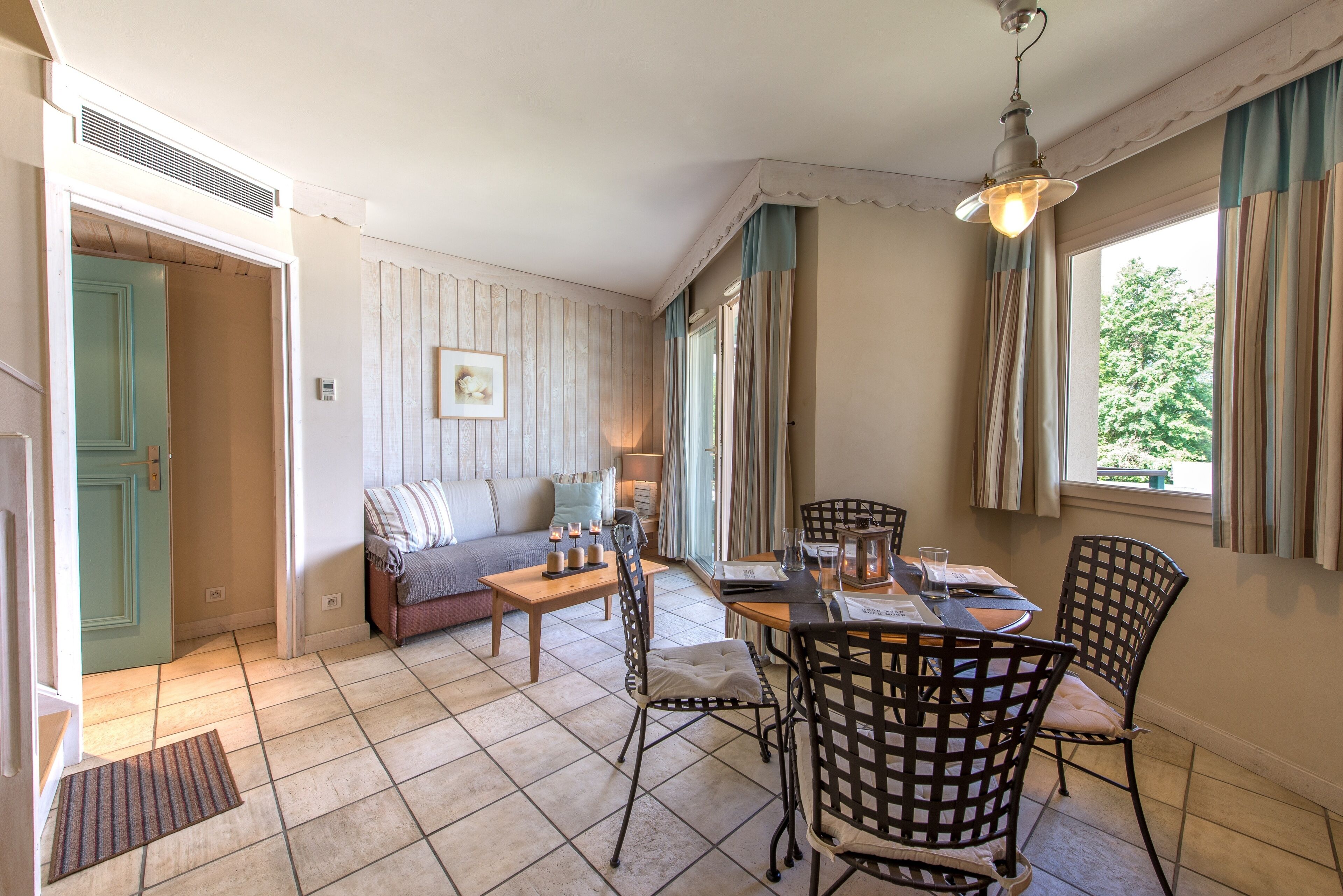 Een gezellige woonkamer met een bank, een eettafel met stoelen, een open haard en een groot raam met gordijnen.