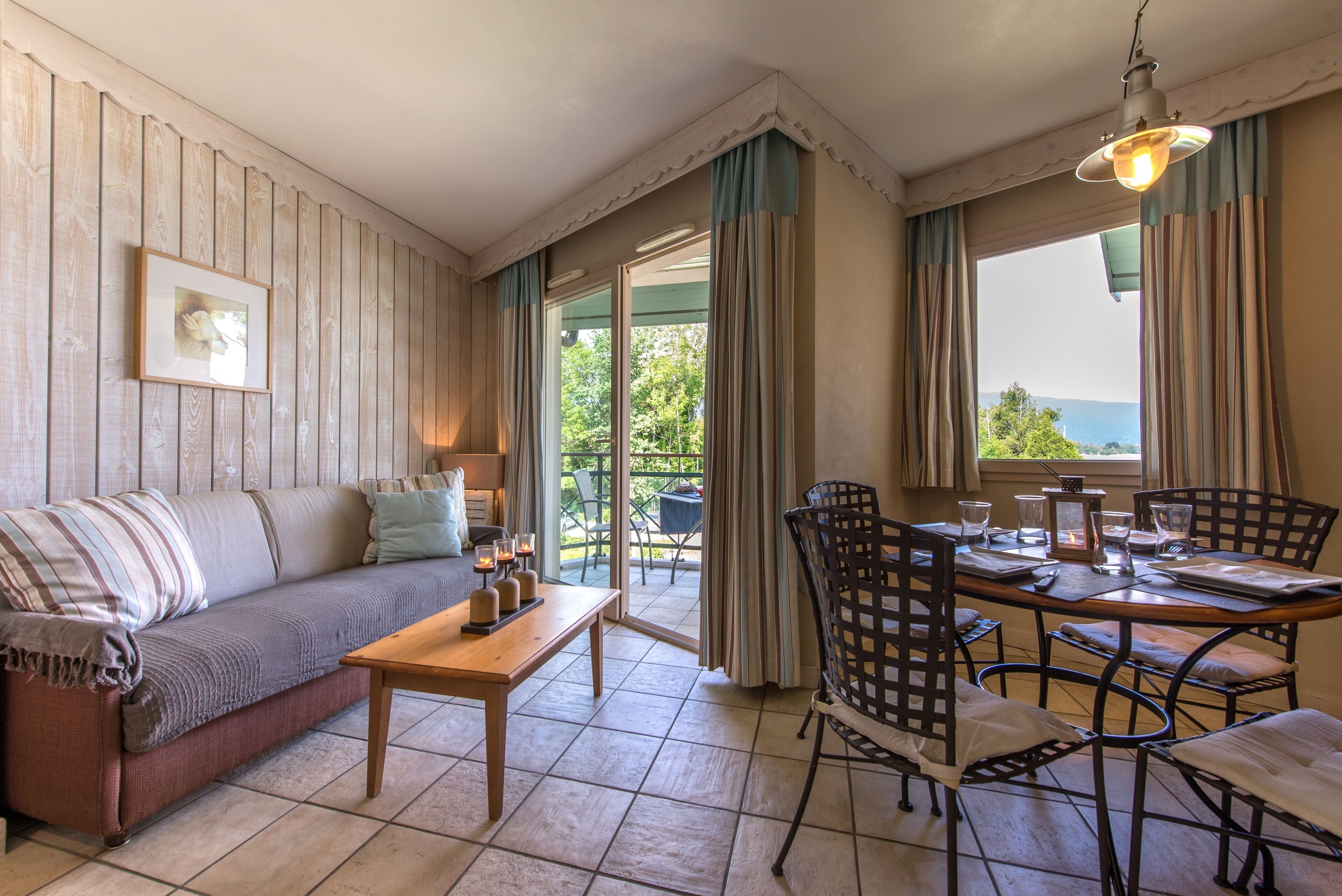 A cozy room with a sofa, a dining table with chairs, and a view of greenery outside.