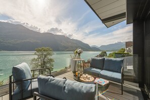 A balcony with a view of a lake and mountains, furnished with a sofa and chairs, and a small table with a vase and a magazine. - Le Cristal - Prestigieux appartement au Lac d'Annecy avec vue unique à 180° (Doussard)