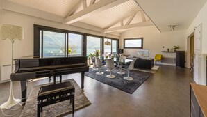 A spacious living room with a grand piano, a dining area with modern chairs, and large windows offering a view of the outdoors.