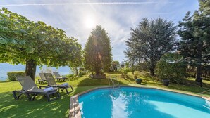 Una piscina con sillones de descanso, rodeada de árboles y vistas al agua.