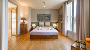 Un dormitorio moderno con una cama grande, dos mesitas de noche con lámparas, un cuadro en la pared y vistas al exterior a través de una ventana.