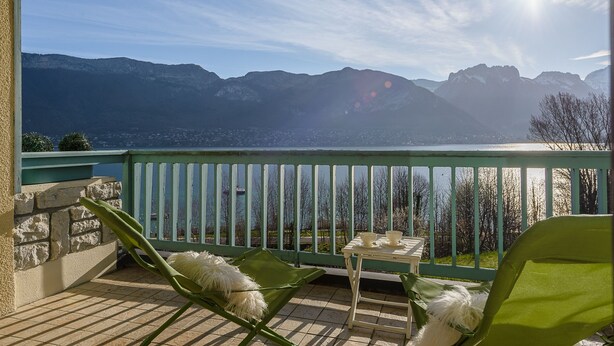 Un balcón con vistas a montañas, una mesa con tazas y una silla con un cojín mullido.