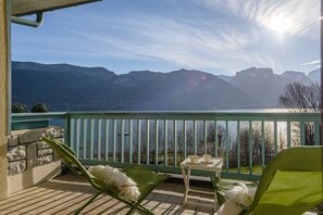 Un balcón con vistas a montañas, una mesa con tazas y una silla con un cojín mullido.