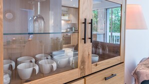 A modern kitchen with wooden cabinets, a glass display case with white mugs, and a view of the outdoors.