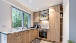A modern kitchen with wooden cabinets, a built-in oven, and a large window providing natural light.
