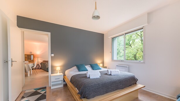 A modern bedroom with a bed, bedside tables, a window, and a view of the outdoors.