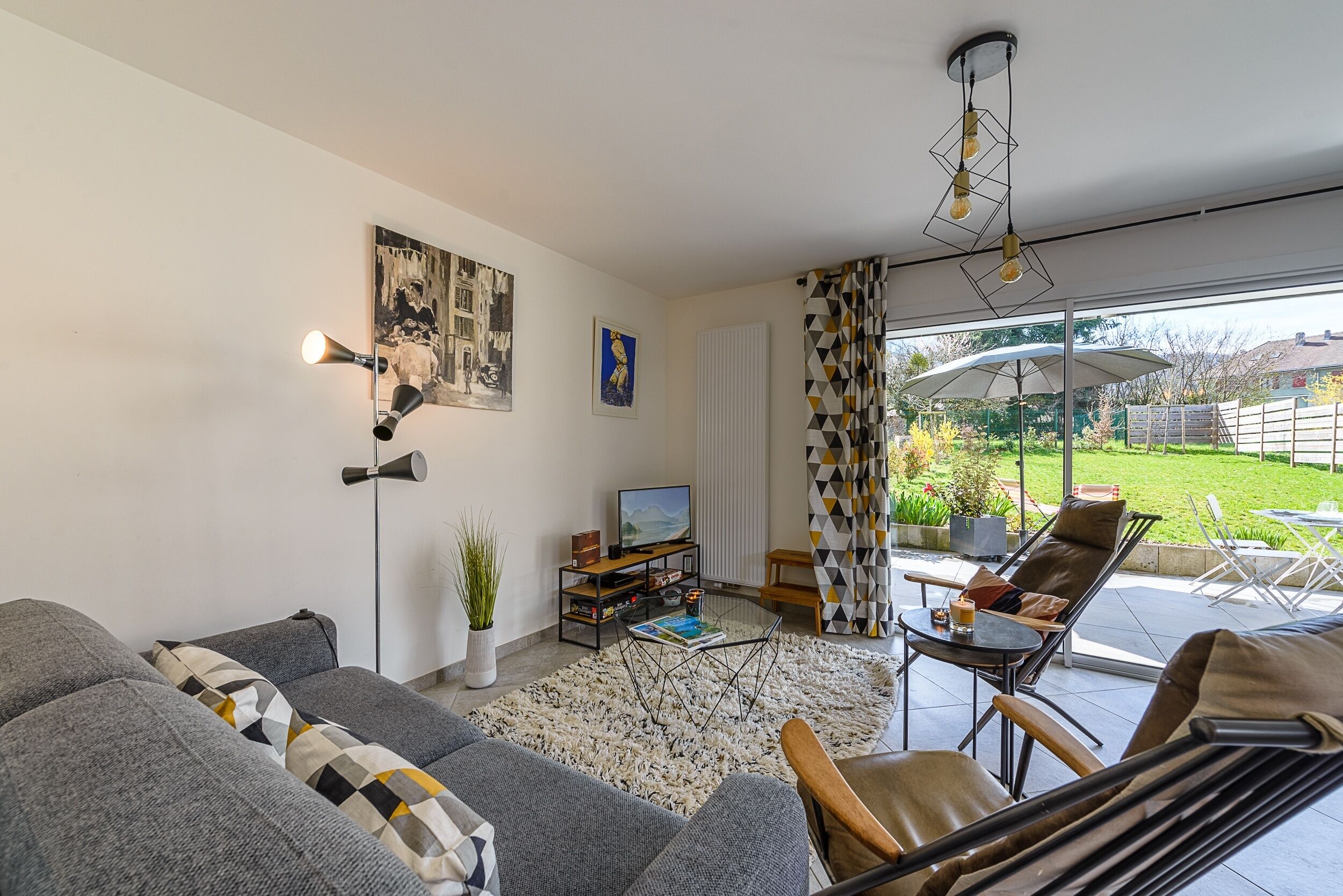 Una sala de estar moderna con sofá, mueble para la televisión y zona de estar exterior con vistas al jardín.