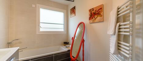 A modern bathroom with a bathtub, a large mirror, and a towel rack.
