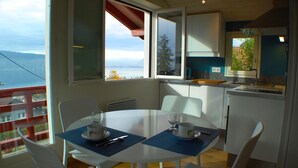 Un comedor con una mesa dispuesta para dos, una cocina con vistas al exterior y un balcón con barandilla.