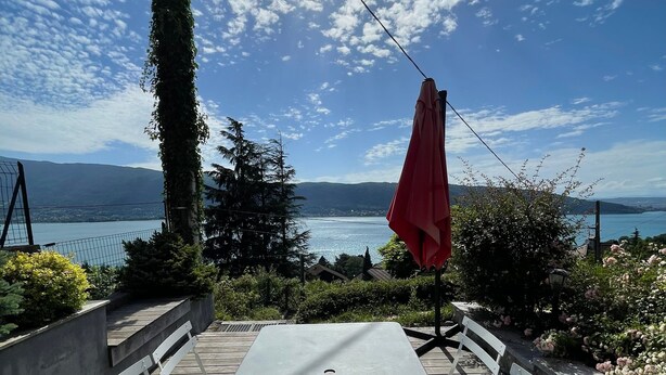 Un patio al aire libre con una mesa y bancos, con vista a un lago y montañas.