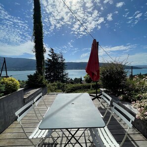 Een terras buiten met een tafel en bankjes, met uitzicht op een meer en bergen.