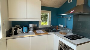 Cocina compacta con armarios blancos, horno integrado, cafetera y ventana con vistas a zonas verdes.