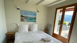 Un dormitorio con una cama grande, un cuadro de una playa y vistas a las montañas a través de una puerta corredera.