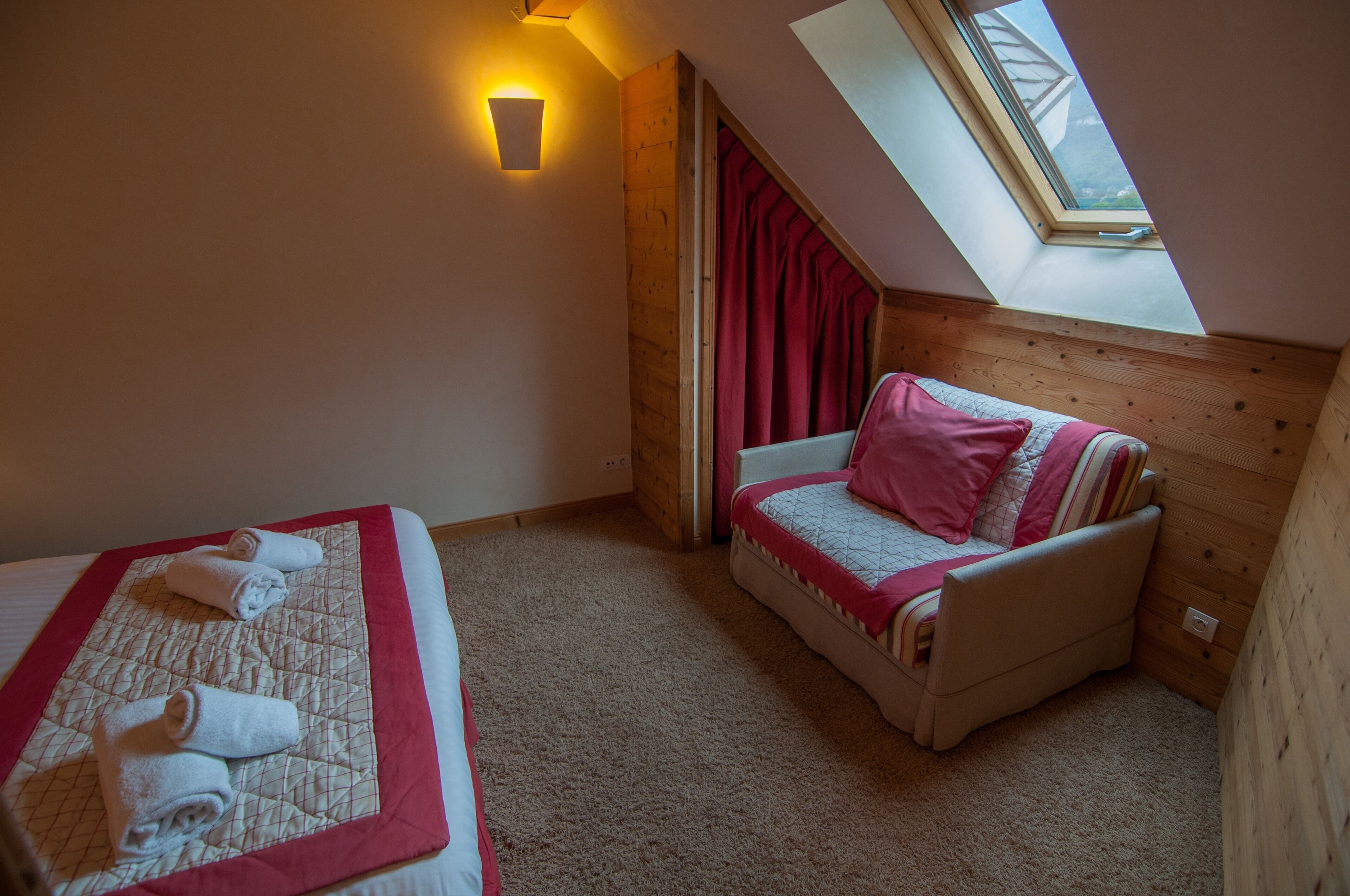 A cozy room with a bed, a sofa, a skylight, and a wall-mounted light fixture.